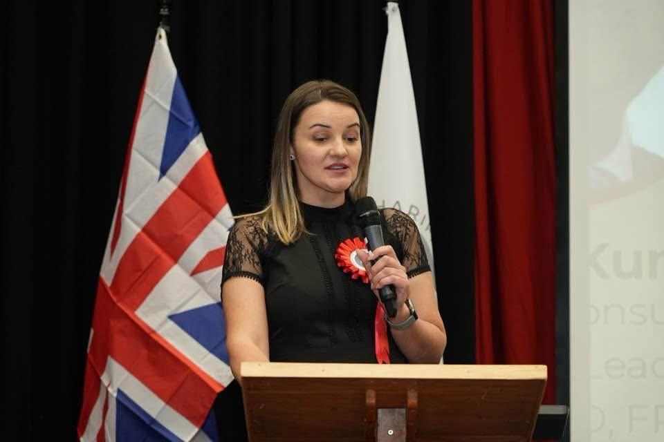 Kristina Culka speaking at a charity event with a UK flag behind the podium